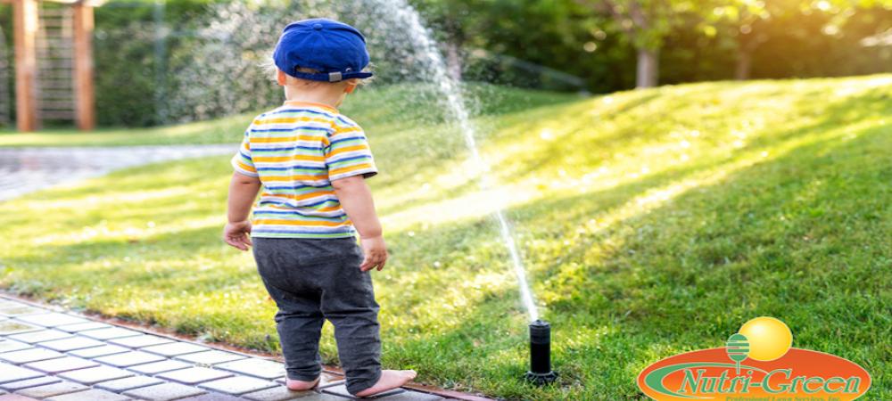 A toddler standing next to a water sprinkler irrigation system. 
